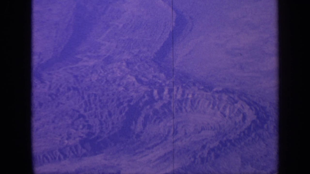 Purple-tinted aerial view of rocky circular terrain with dark film borders.