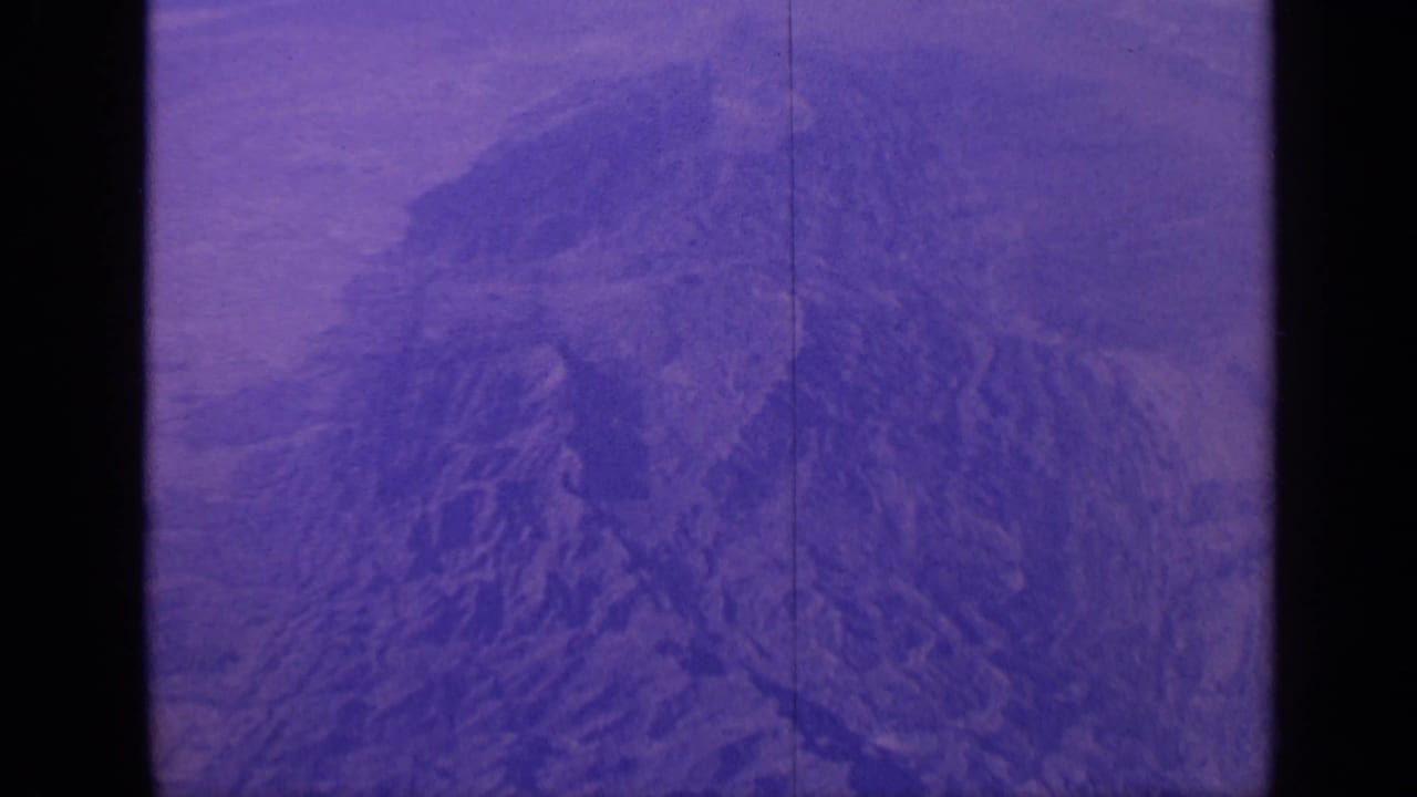 1970 India 8mm frame showing a purple-blue aerial view of rugged mountain terrain with a visible film split and soft grain.