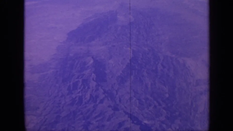 1970 India 8mm frame showing a purple-blue aerial view of rugged mountain terrain with a visible film split and soft grain.