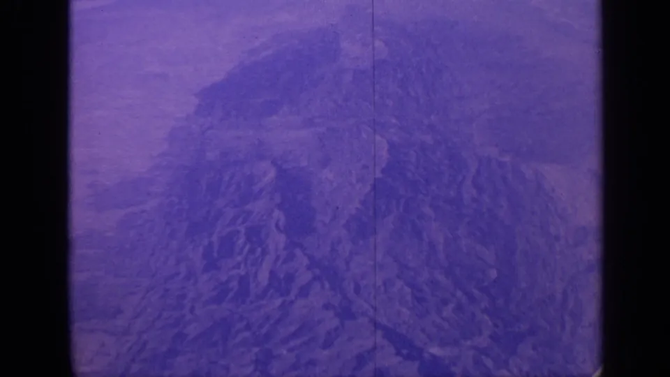 1970 India 8mm frame of rugged mountain ridges seen from above, with strong purple-blue aging and visible film borders.