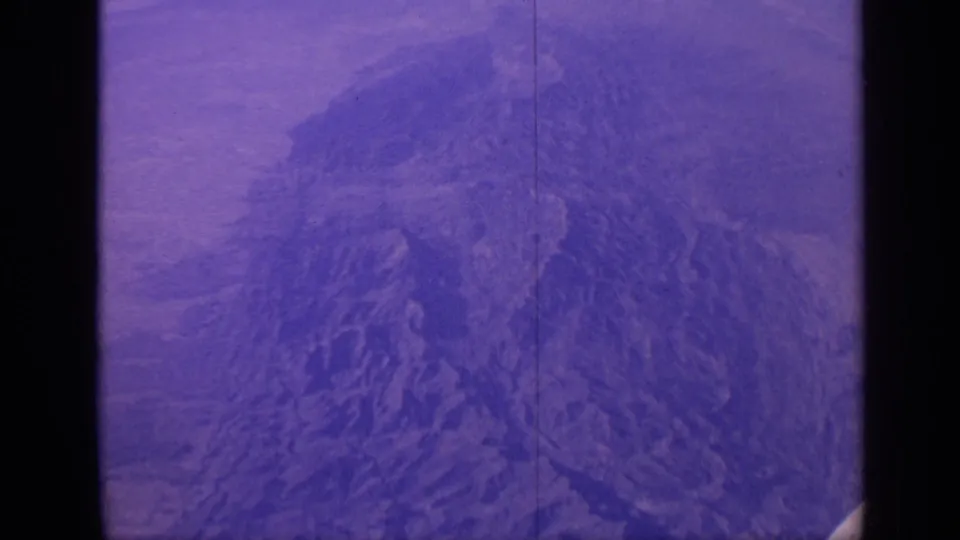 1970 India 8mm frame showing a softened aerial view of a rocky mountain formation, tinted purple by aged film stock.