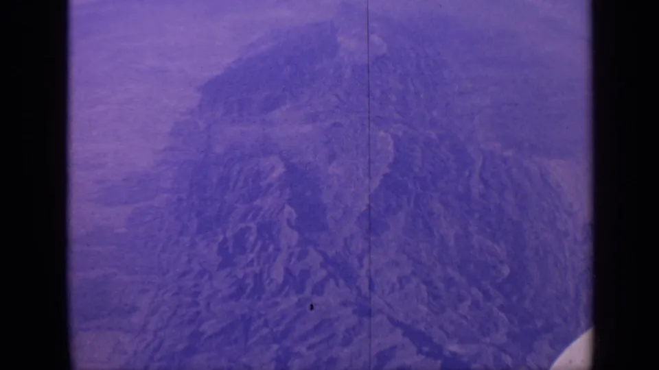 1970 India 8mm frame of jagged terrain from above, showing pronounced grain, purple-blue tones, and edge artifacts from the film scan.
