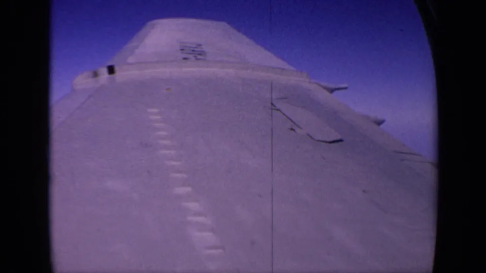 1970 India home-movie frame with the aircraft body and wing surface viewed close up against the sky.
