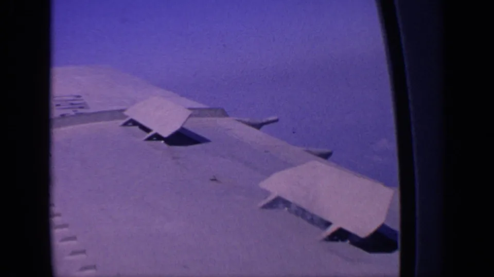 Large airplane wing and raised flap panels appear through the aircraft window in this 1970 India home-movie frame.