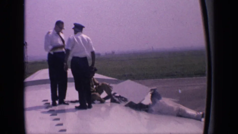 On a large aircraft wing in India, two uniformed officers appear to talk as a maintenance worker adjusts or inspects the flap area.
