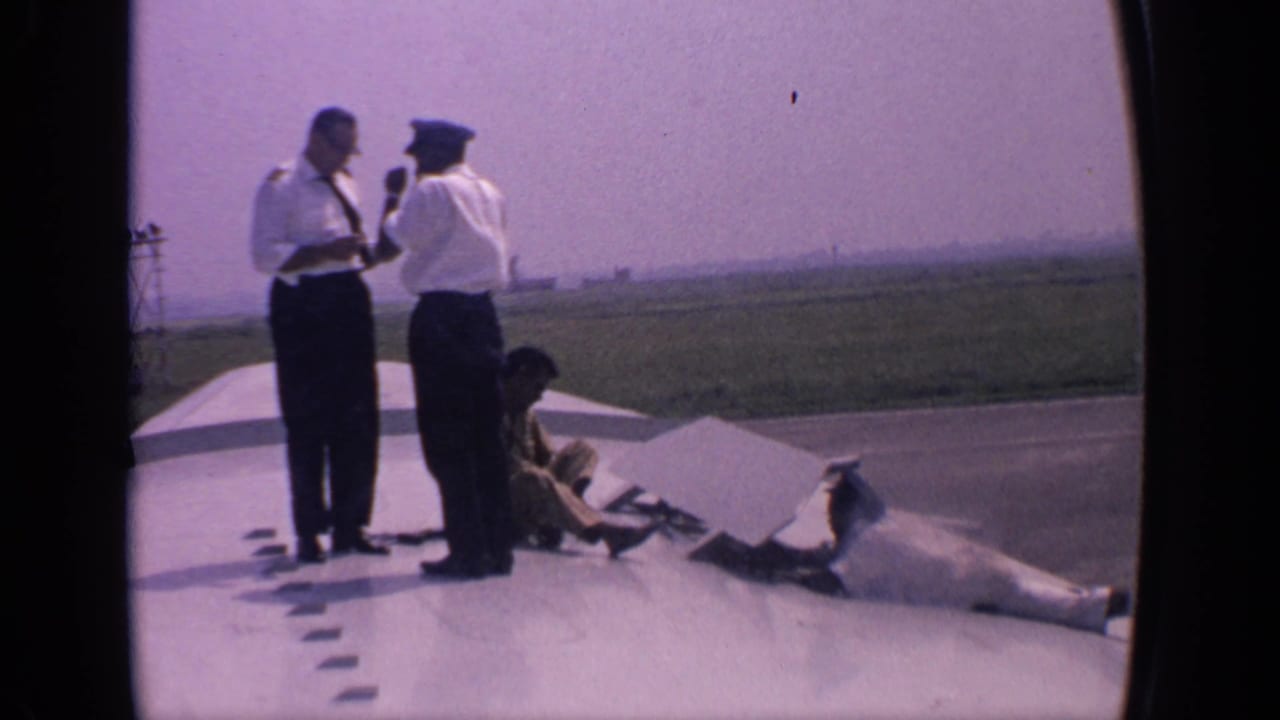 Two uniformed airline crew members stand on an aircraft wing while a worker crouches nearby.