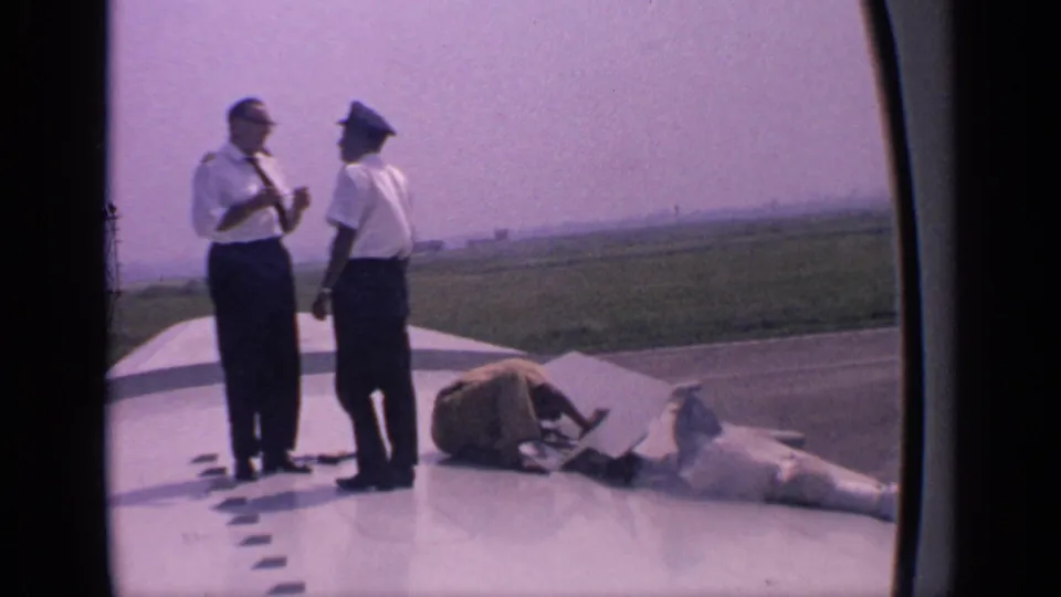 Two airline crew members in uniform stand on a parked aircraft wing in India, with a maintenance worker crouched near equipment at their feet.