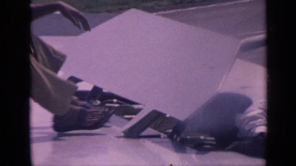 Close 8mm view of a parked aircraft wing in India showing a crouched worker, a loose panel or cover, and small tools or components.