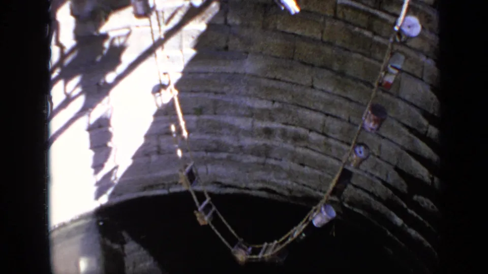 Stone well structure with ropes, pulley lines, and hanging containers, filmed in India in 1970 on 8mm stock.