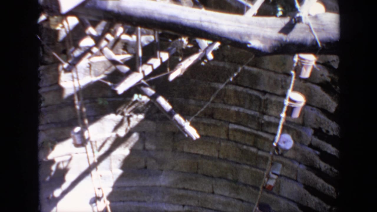 Large wooden wheel parts and beams beside a weathered brick wall.