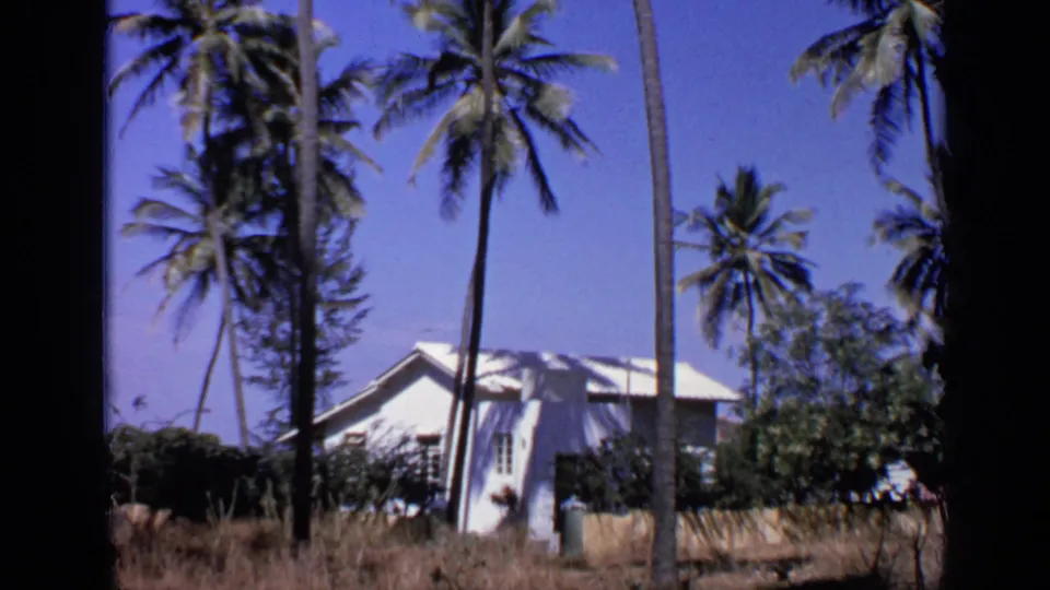 Another 1970 India home-movie view of the palm-shaded white building, with dry ground and soft 8mm color.
