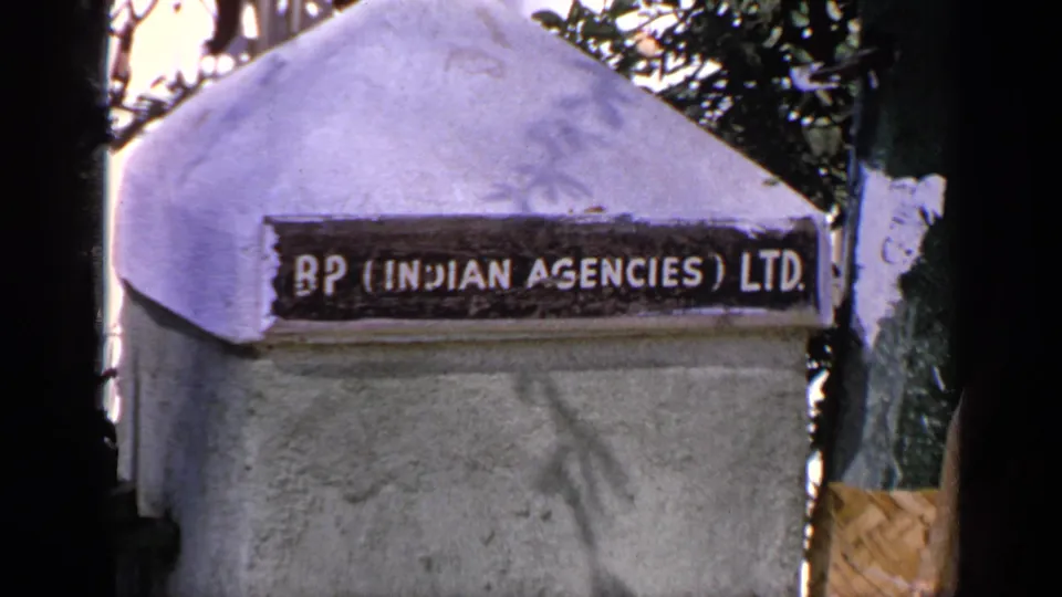 1970 India frame centered on the BP (Indian Agencies) Ltd sign, with textured concrete, foliage, and edge shadows visible.