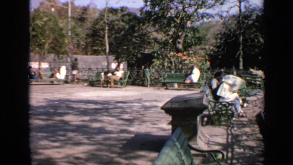 1970 India frame with benches, pedestrians, trees, and a shaded walkway in a public area.
