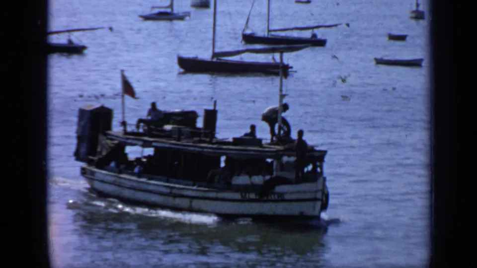 India 1970 8mm frame showing boats on blue water, with several people silhouetted aboard the nearest vessel.