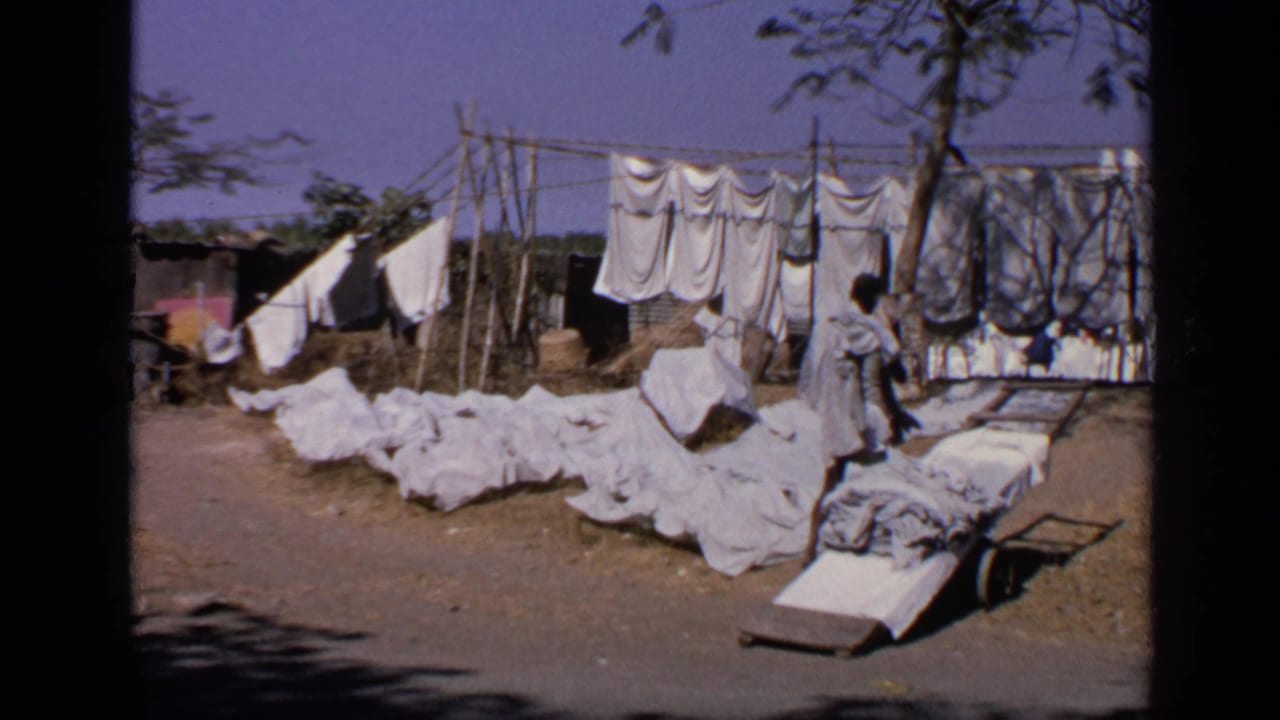 White laundry hangs and lies on dirt ground beside wooden poles and simple shelters.