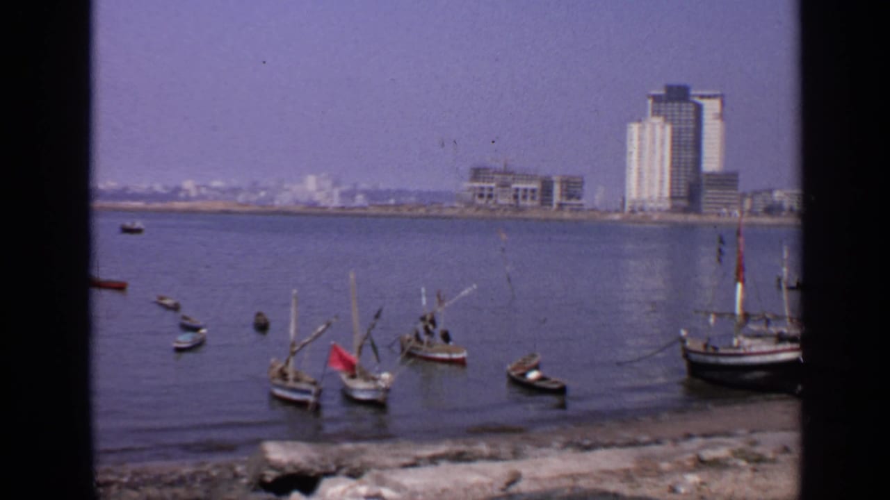 Small boats on calm coastal water with distant waterfront buildings.