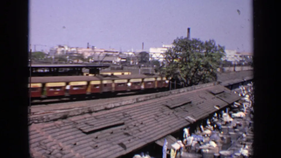 Elevated 1970 India view of train cars passing beside a market crowded with people and goods.