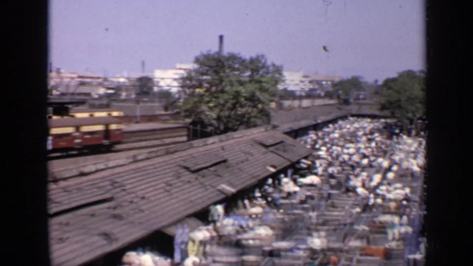 1970 India 8mm frame with the rear of a passing train and a crowded open-air market below.