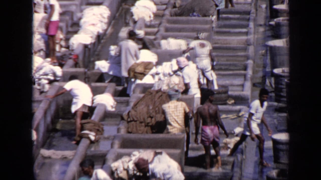 Workers wash and carry fabrics beside stepped concrete washing basins.