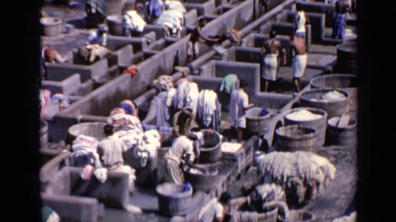 Overhead 1970 India 8mm view of people working among concrete laundry cubicles, tubs, wet basins, and piles of fabric.