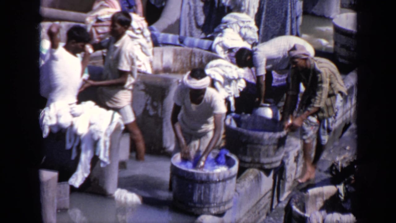 Men washing clothes by hand in wooden tubs surrounded by piled laundry.