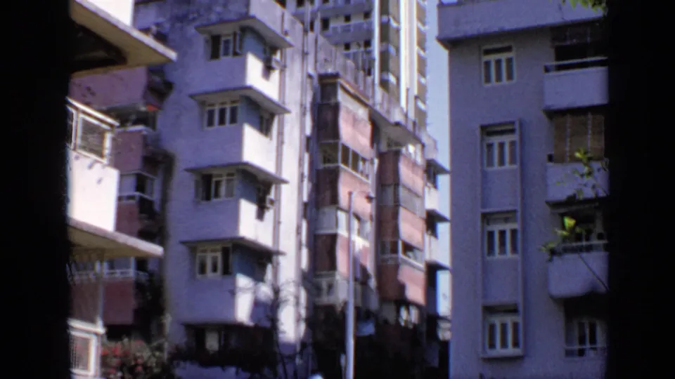 1970 India home-movie frame with closely framed apartment or hotel facades, balconies, windows, and shadowed film edges.