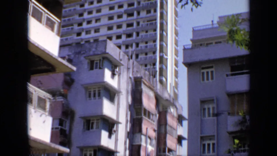 1970 India 8mm frame looking upward at adjacent apartment or hotel buildings with balconies, windows, and a taller block behind.
