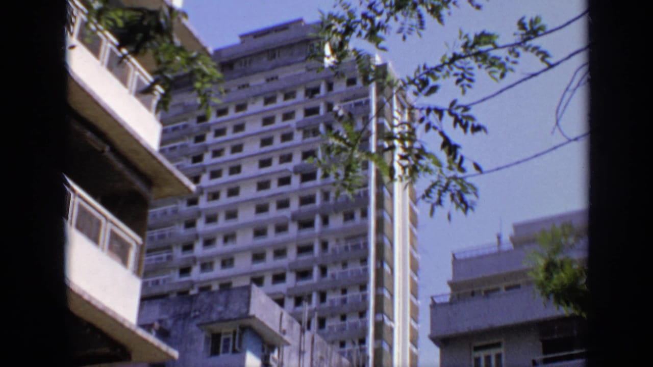 White apartment buildings seen past trees and dark film-edge shadows.