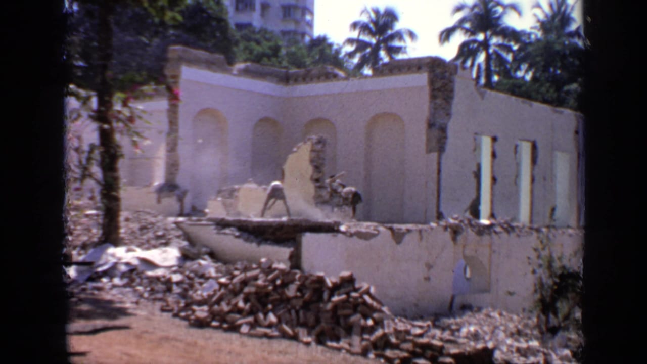 Damaged wall and rubble in bright sun with a worker bending near the structure.