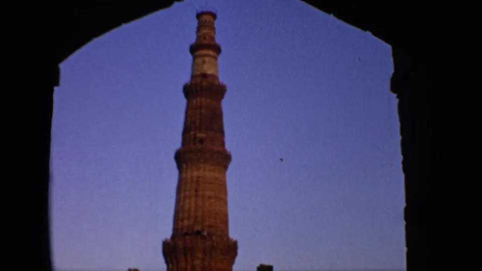 1970 India home-movie frame showing the Qutub Minar framed by a shadowed arch, continuing the landmark view from a visitor perspective.