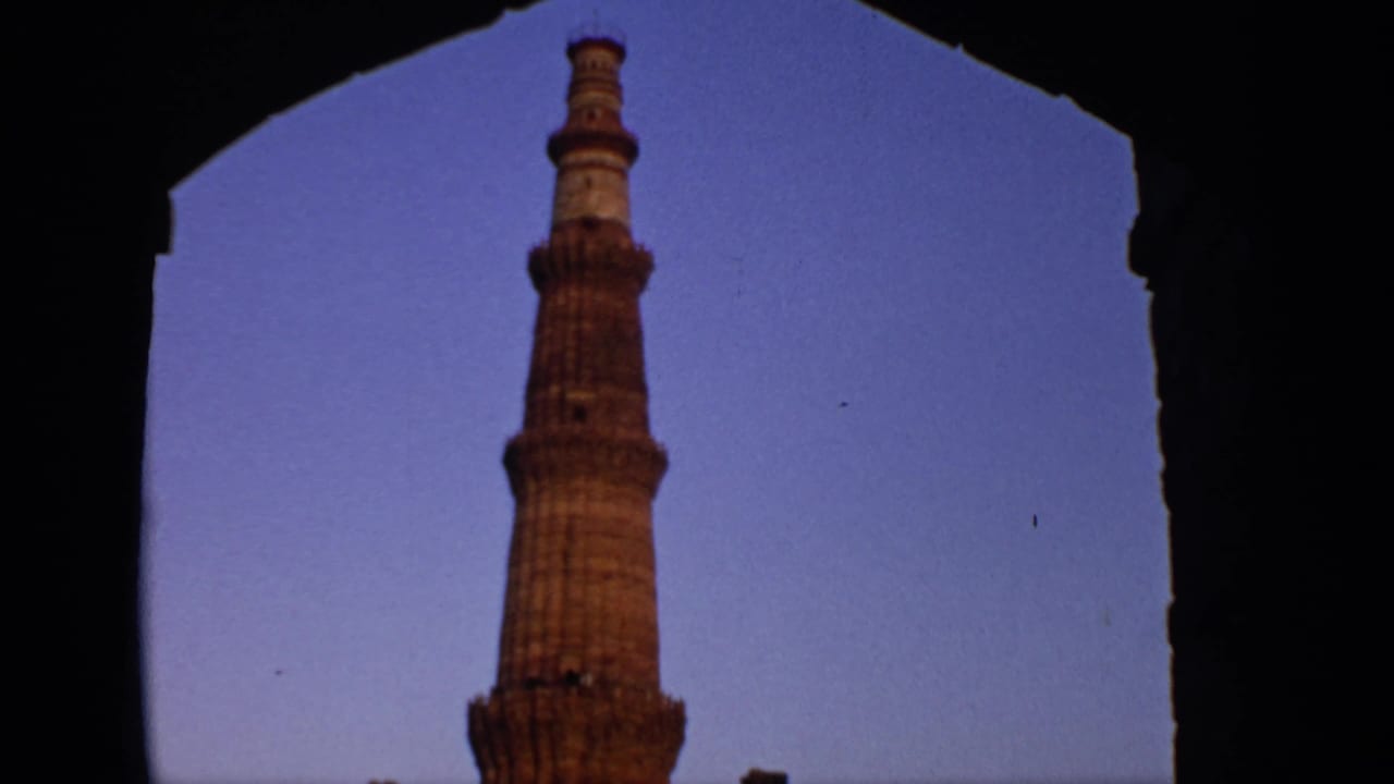 Qutub Minar seen through a dark stone arch against a blue-purple sky.