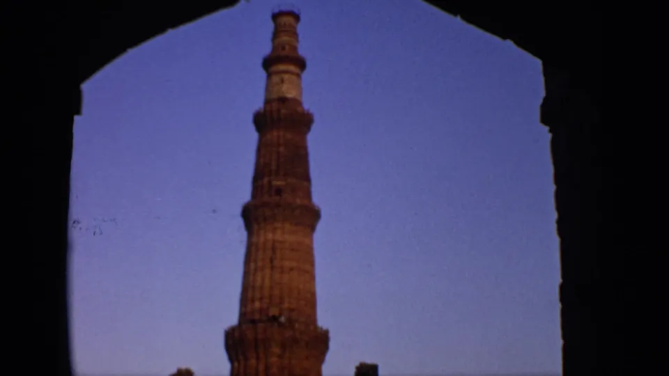 Qutub Minar in Delhi appears through a shaded archway, with the tower rising against a clear blue-purple sky.