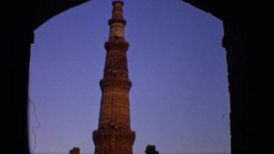 The 8mm frame holds a closer view of Qutub Minar, partly enclosed by a shadowed stone arch and blue sky.