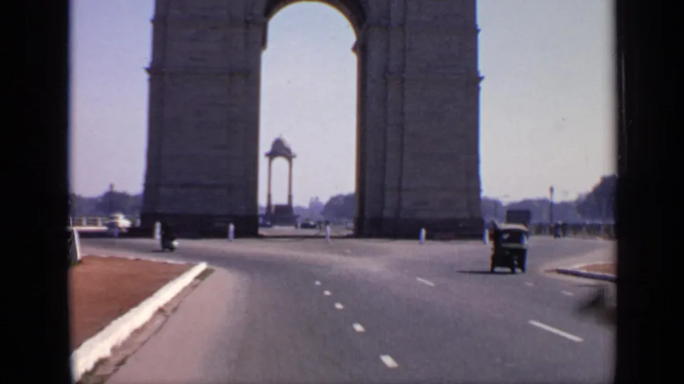 1970 Delhi view of India Gate from the roadway, with the stone arch framing a distant monument and light traffic in the foreground.