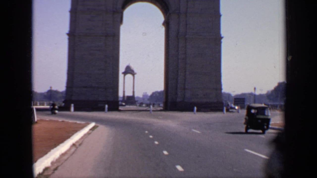 1970 8mm view near India Gate in New Delhi, with a wide road, sparse vehicles, and the memorial arch dominating the frame.
