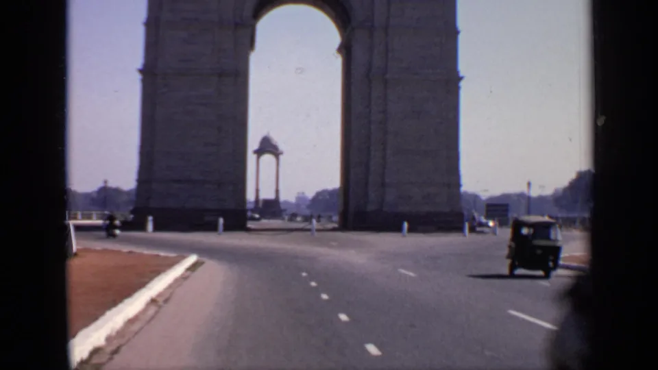 1970 8mm view near India Gate in New Delhi, with a wide road, sparse vehicles, and the memorial arch dominating the frame.