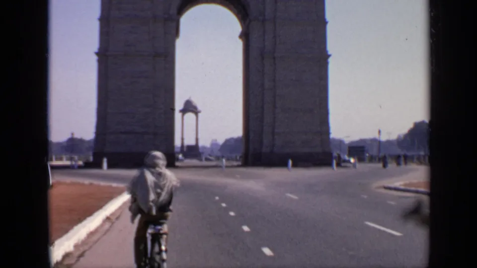 A cyclist moves along the road near India Gate in New Delhi, with the arch, curb, and a few distant vehicles visible.