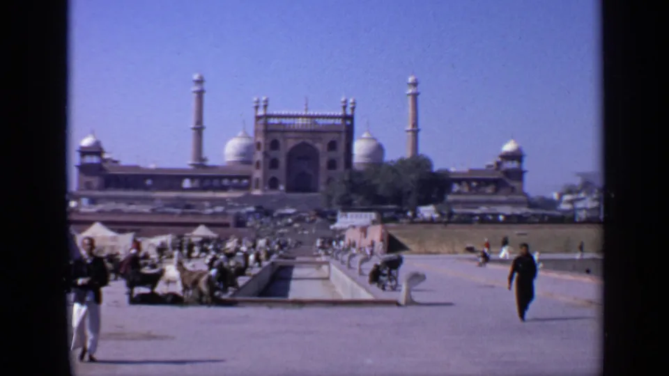 1970 India 8mm frame showing a large domed historic building with minaret-like towers, open paving, and pedestrians in front.