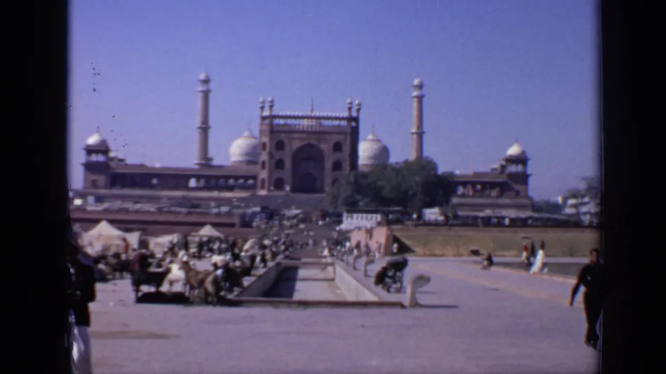 1970 India 8mm frame of visitors and animals in an open courtyard leading toward a domed mosque with minarets under a bright sky.