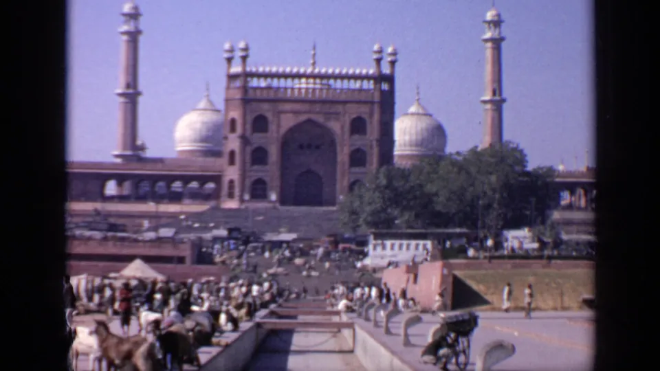 1970 8mm footage in India shows a crowded approach to a mosque, with animals, steps, trees, domes, and minarets visible.