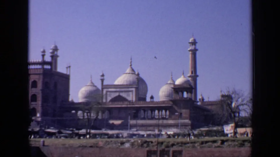 1970 India 8mm view of a prominent mosque with white domes, minarets, arched facade, open ground, and small distant figures.