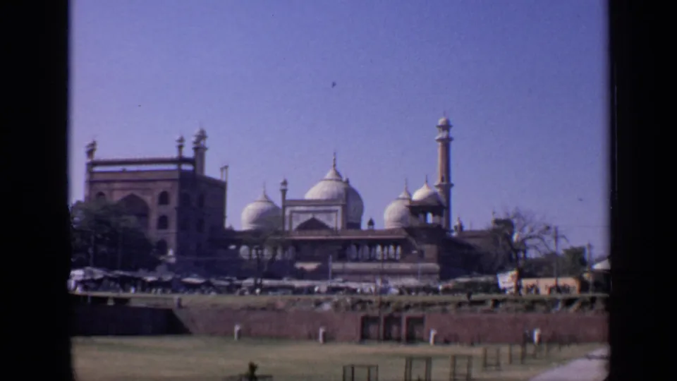 1970 8mm view in India showing the Taj Mahal complex with domes and minarets beyond a grassy foreground and low wall.