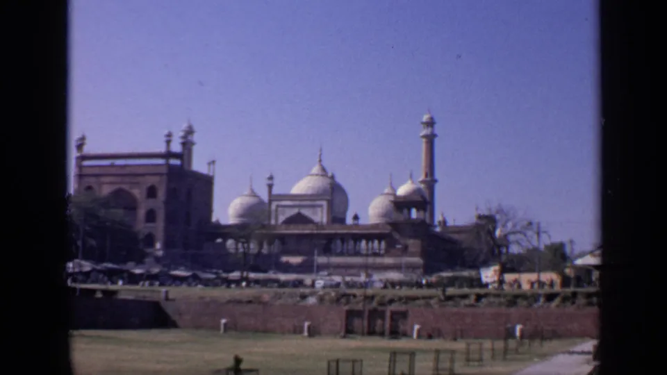 1970 home-movie frame of the Taj Mahal area in India, seen from a distance with people and stalls along the lower edge.