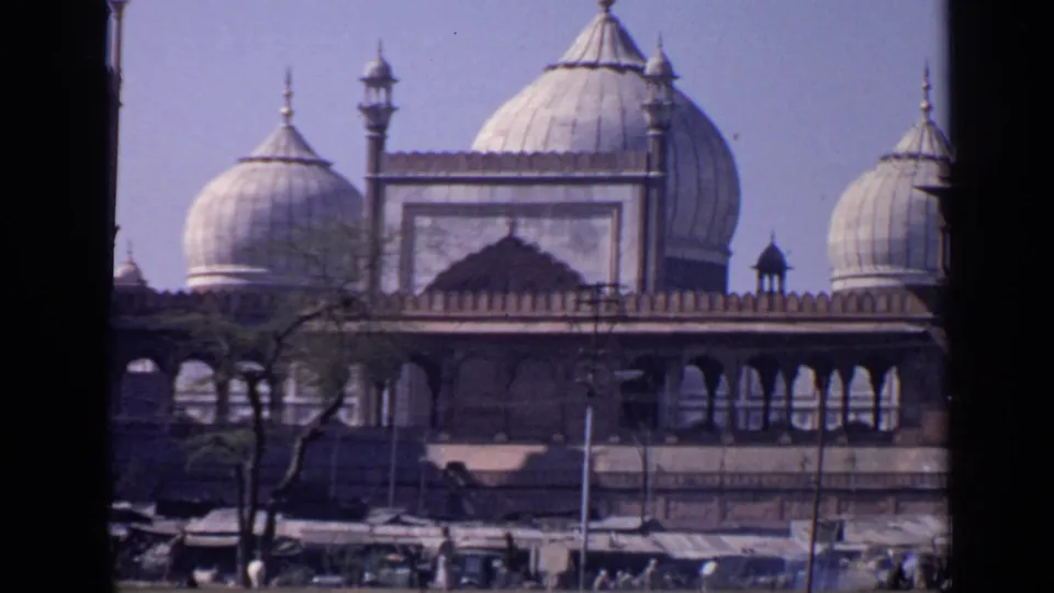 Closer 1970 8mm view of the Taj Mahal complex in India, with domes, arcade, trees, stalls, and small visitors below.