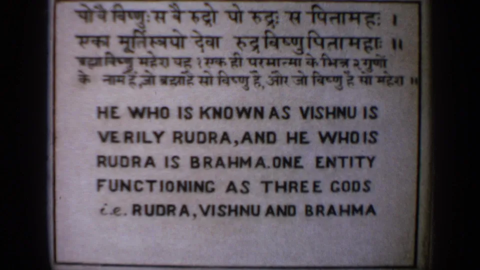 Close 8mm frame of a bilingual sign stating that Rudra, Vishnu, and Brahma are one entity functioning as three gods.