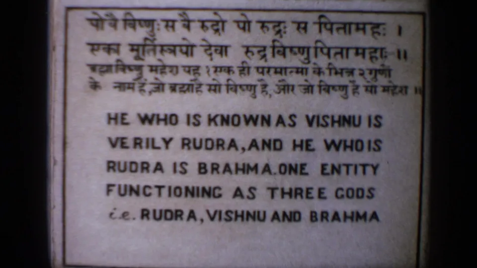 1970 India 8mm frame with a slightly shifted view of the bilingual Hindu trinity text placard and visible film softness.