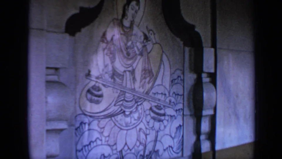 1970 India 8mm frame showing a carved seated Hindu deity with a stringed instrument, lotus base and surrounding niche details.