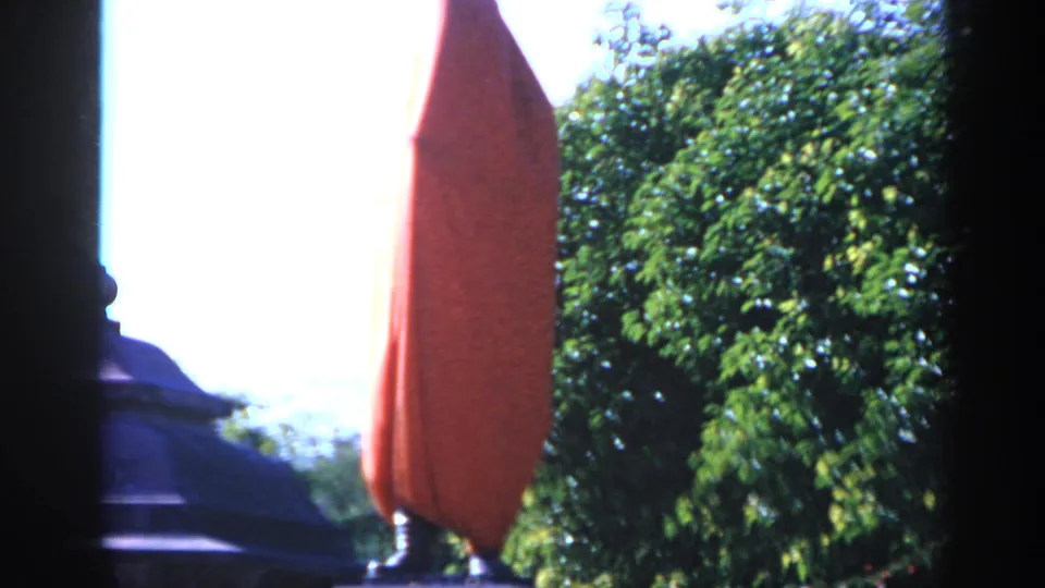 1970 India 8mm frame showing a statue or form draped in red cloth outdoors, with trees and bright daylight behind it.