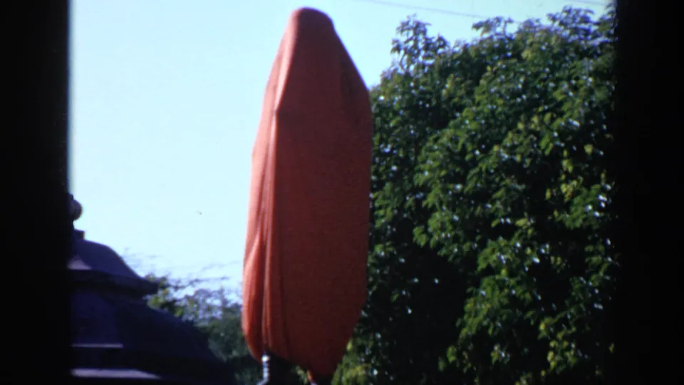 1970 India 8mm frame showing a red-covered vertical object near dense green trees and a dark frame edge.