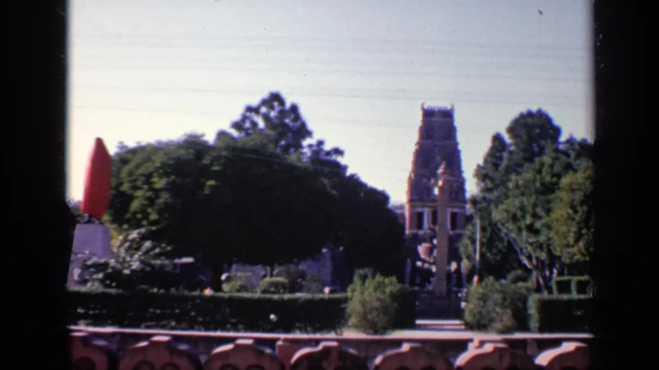 The final frame keeps the tower, trees, hedges, and garden path in view while the red-covered object sits partly off to the left.